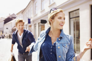 Gorgeous young woman and man walking along shops holding hands